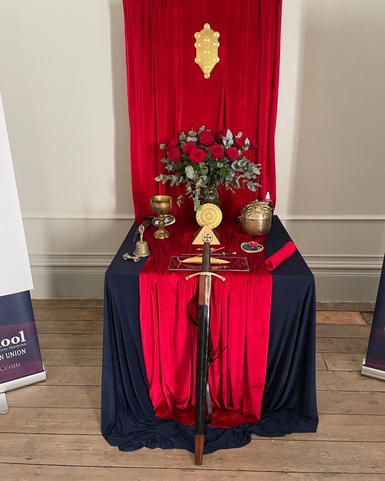 A ceremonial altar with red velvet, a gold Tree of Life, roses, and a sword