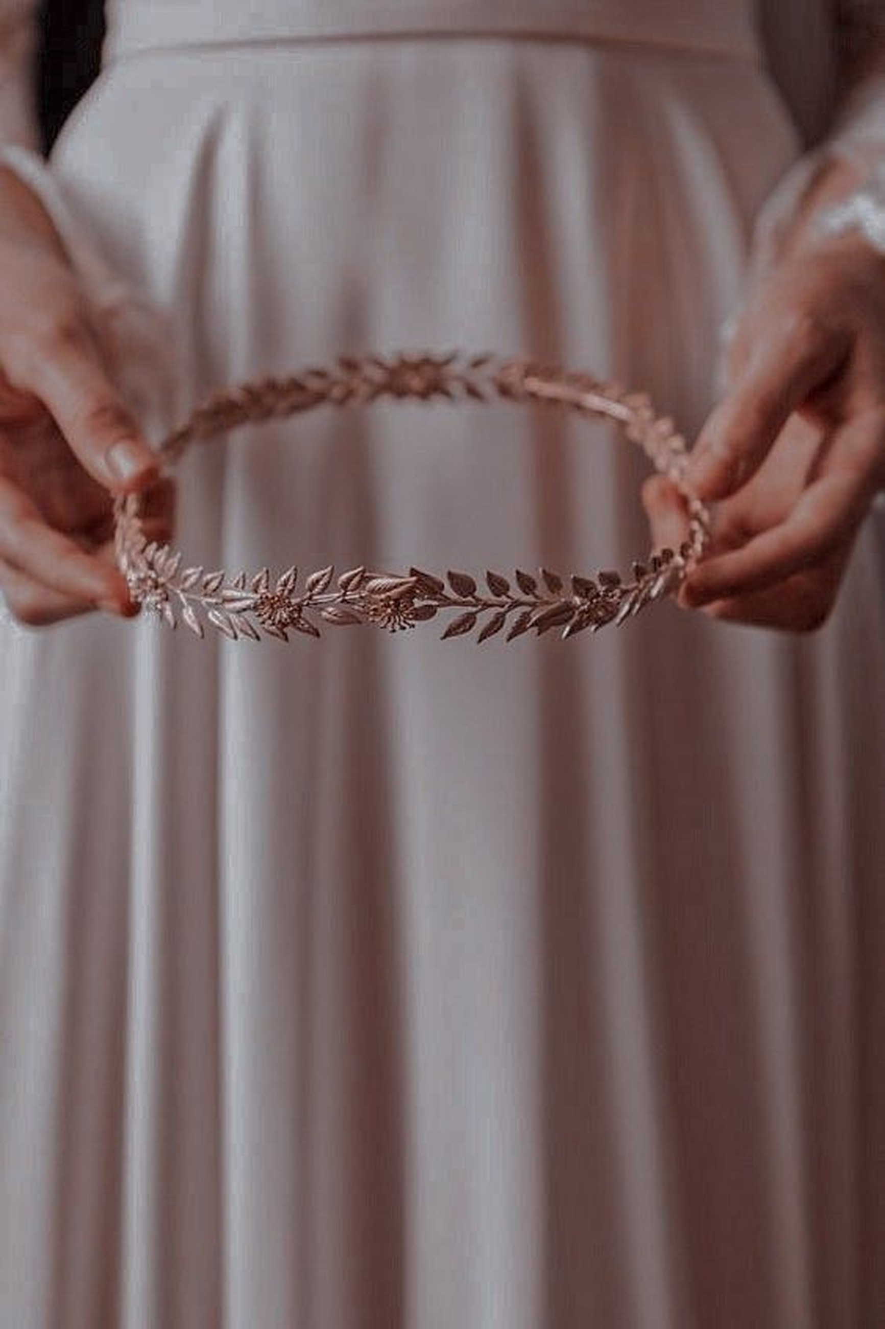 A rose gold laurel crown held between two hands